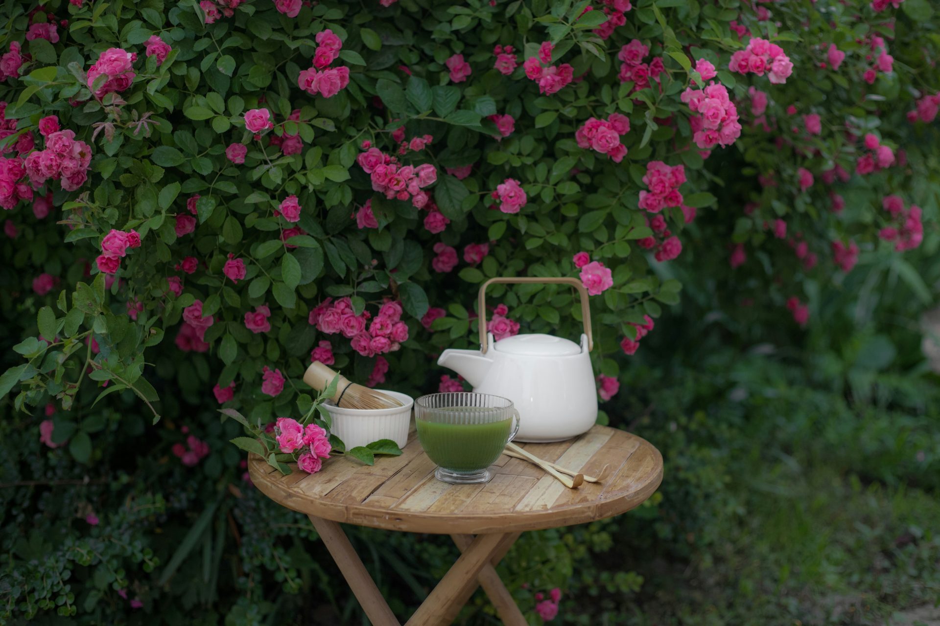 Tea set arranged on a table in front of pink roses.